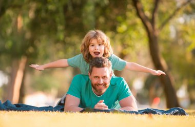 Baba, küçük oğlunu çimlerin üzerinde yatarken sırtında taşıyor. Babalar Günü konsepti