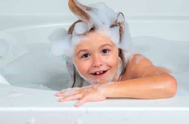 Sabun köpüklü banyo küveti. Küvette köpükle oynayan tatlı sarışın çocuk. Mutlu çocuk gülümsüyor ve kameraya bakıyor. Tasasız çocukluk. Küçük çocuk büyük miktarda köpükle banyo yapıyor.