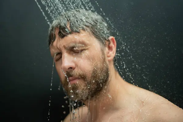 Man washing hair in bath. Guy bathing shower head in bathtub. Face in foam in shower. Bathing man taking shower. Close up guy showering. Shower concept. Man is under water drops in showers
