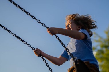 Çocuk yüksekten sallanıyor. Sevimli sarışın çocuk parkta salıncakta sallanırken eğleniyor. Oyun alanında sallanan mutlu çocuk. Yaz oyun parkı. Yüksekten sallanan çocuk