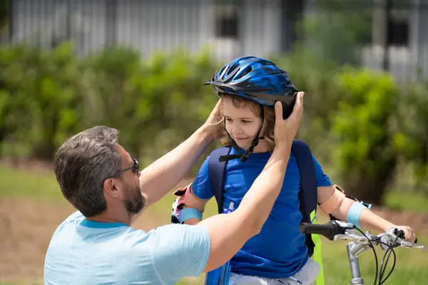 Fathers day concept. Father and son in bike helmet learning ride bicycle. Father and son on bicycle on summer day outdoor. Father helping his son to wear a cycling helmet. Happy fathers day