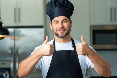 Mutlu aşçı baş parmağı yukarıda. Mutfakta şef şapkası takmış şefin portresi. Önlük, şef üniforması ve aşçı şapkası takan bir adam. Karakter mutfakçısı, reklam şefi.