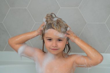 Yüzü köpüklü çocuklar gibi. Şampuan köpüğü ve banyo yapan saçlarında kabarcıklar olan bir çocuk. Gülümseyen çocuk portresi, saç bakımı ve hijyen konsepti. Çocuklar uzun saçlar için şampuan kullanırlar. Banyoda saç yıkamak.