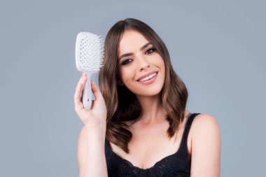 Saçlarını tarayan gülümseyen bir kadın. Uzun saç fırçası olan güzel kız.