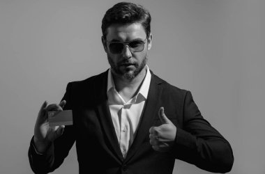 Ciddi kibirli bir iş adamının gri arka planda plastik kredi kartı gösteren portresi. İş ve başarı kavramı. İnternetten alışveriş. Çevrimiçi ödeme. Kredi kartının bakiyesi