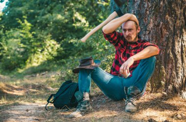 Ormanda oturan oduncu adam. Yasadışı günlük bugün devam ediyor. Ormanda baltayla duran oduncu işçi. Tarım ve ormancılık teması. Oduncu ormanda balta ile ayakta
