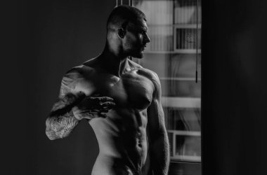 Pencere perdeleri üzerinde şehvetli kaslı iri kıyım bir oda. Yatak odasında kaslı üstsüz erkek modeli. Gay seksi kas modeli. Güçlü omuzlar ve göğüs. Çıplak gövdeli kaslı seksi adam. Atletik vücut