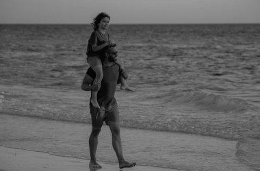 Baba ve oğlu o gün kumsalda yürüyorlardı. Mutlu bir aile. Babalar Günü. Aşk ailesi, baba ve bir çocuk yaz tatilinde deniz sahilinde birlikte yürürler. Oğul babasının omuzlarında sırtımda