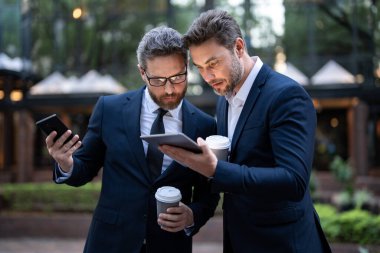 İş görüşmesi. İş adamı tecrübesini paylaşıyor. İş ortakları kahve molasında tablet kullanıyor, dışarıda buluşuyorlar. Formaliteleri tartışan iki kendine güvenen iş adamı.