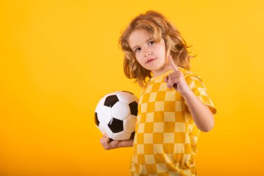 Çocuk çocuk klasik futbol topunu sarı stüdyoda izole bir şekilde tutuyor. Stüdyoda elinde futbol topu tutan çocuk. Çocuk topla oynuyor. Spor, çocuklar için futbol hobisi. Futbol topuyla poz veren küçük bir futbolcu