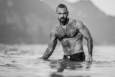 Adam gölde rahatladı. Yaz plajında çıplak gövdeli yakışıklı bir adam. Alps gölündeki seksi bir adamın portresi. Özgürlük ve seyahat macerası. Seksi gezgin İsviçre 'de manzaranın tadını çıkarıyor