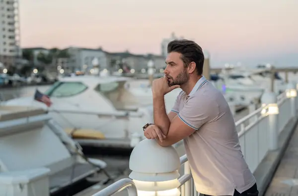Rich business man dreaming and thinking near the yacht. Urban fashion man in city walking street. Portrait of stylish handsome man outdoors. Portrait of attractive man walking on the street