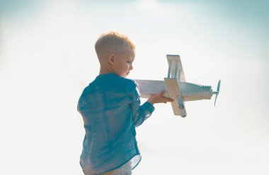 Tahta oyuncak uçakla oynayan çocuk pilot olma hayali kuruyor. Çocuk rüyaları. Ahşap uçaklı çocuk pilot. Çocukluk hayali kavramı