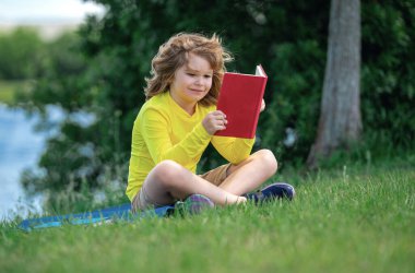 Akıllı çocuk dışarıda parkta kitap okuyor. Yazın kitap okuyan sarışın çocuk. Zeki çocuklar açık hava portresi. Çocukların hayal gücü, yenilik ve ilham kaynağı. Açık okul, öğrenen çocuklar.