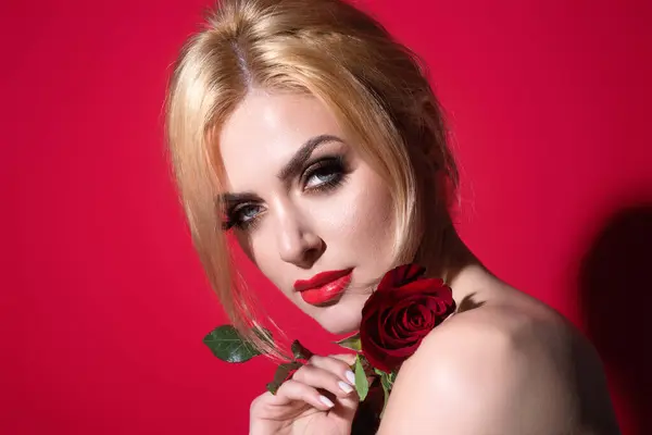 赤いバラを持っている魅惑的な女性 赤いバラの花と美しいモデル 赤いスタジオの背景に隔離されています 完璧なメイクで魅力的な若い女の子 — ストック写真