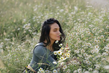 Papatya tarlasında eğlenen seksi kadın. Yaz papatya çiçeklerinin çayırında yatan güzel bir dişi. Yazlık çim tarlasında güzel bir kız. Esmer model ve yaz yeşili doğa, uyum kavramı.