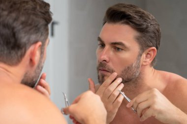 Tıraş olduktan sonra mükemmel cilt teması olan çekici bir adam. Cilt bakımı kozmetik işlemleri konsepti. Aynaya bakan adam, hassas cilt, kozmetik tedavisi. Cilt bakımı