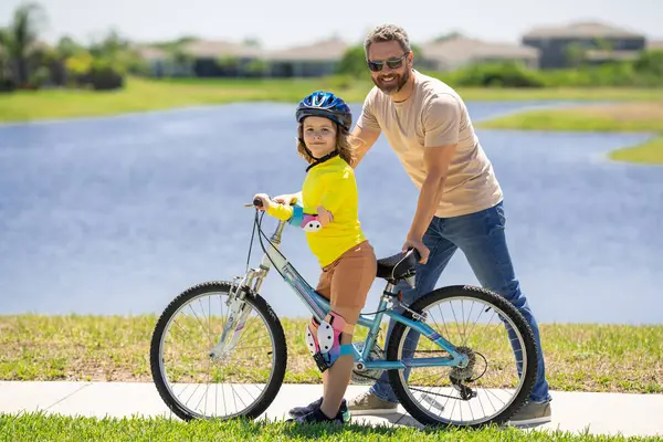 Happy Fathers day. Father teaching son riding bike. Father helping excited son to ride a bicycle in american neighborhood. Child in bike helmet learning to ride cycle with his dad. Fathers day