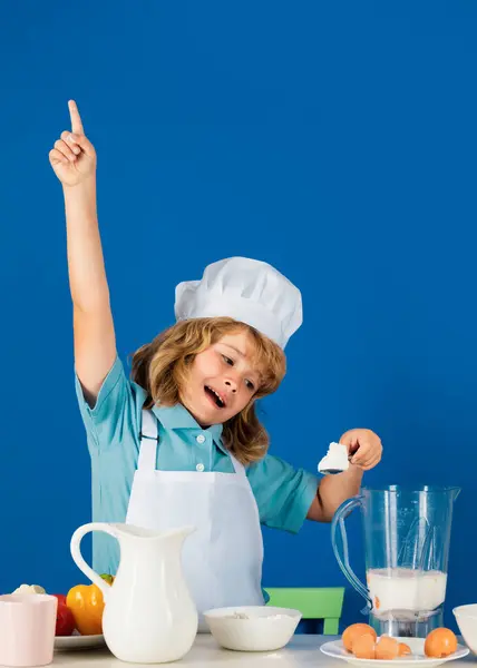 Excited funny chef cook. Portrait of a 7, 8 years old child in cook cap and apron cooking food with flour in kitchen. Cute little blonde happy smiling chef