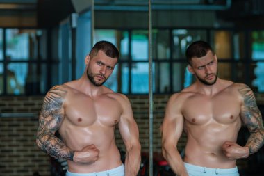 Spor salonunda poz veren kaslı iri kıyım. Spor aletlerinin yanında fitness mankeni. Genç kaslı adam egzersizi. Spor salonundaki güçlü kaslı adam. Spor ve motivasyon. Ağırlıkla egzersiz yapar