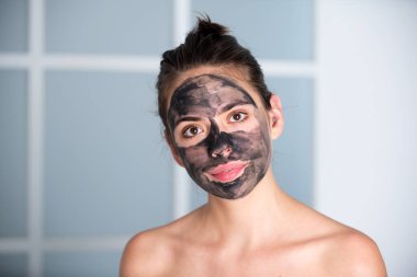 Woman with charcoal facial mask. Beautiful young woman with facial black mud clay mask. Skin care and treatment, spa, natural beauty and cosmetology concept