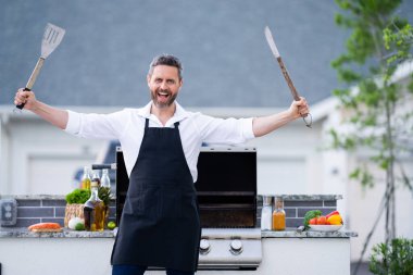 Yakışıklı adam dışarıda barbekü ızgarası hazırlıyor. Adam arka bahçede ızgarada lezzetli yemekler pişiriyor. Şef barbeküde yemek hazırlıyor. Milenyum adamı ızgarada et pişiriyor. Barbekü partisi. Izgara yemek.