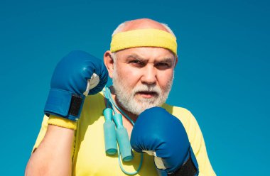 Yaşlı adam boks - yakın portre. Boks tekmesi pratiği yapan yakışıklı yaşlı adam. Kıdemli sporcu boks eldiveni giyiyor. Boks pozisyonunda duran komik sakallı adam. Savaşçı.