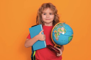 Bilgi toplama günü. Okullu çocuk, sarı stüdyo arka planında izole edilmiş dünya küresi ve kitabı tutuyor. Okul ve çocuklar. Kitap okuyan sevimli sarışın çocuk. Bilgi günü