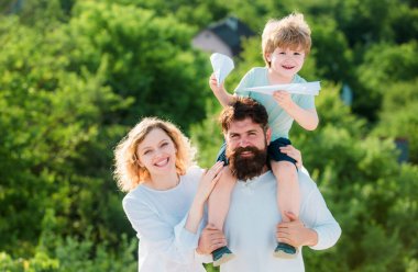 Baba, anne ve oğlu gökyüzü arka planında oynuyorlar. Mutlu bir çocuk ve anne babası yaz mevsiminde arka planda oyuncak kanatlarla oynuyorlar. Baba, anne ve bebek dışarıda birlikte oynuyorlar.