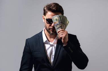 İyi ödeme. Yakışıklı adam gri stüdyoda izole edilmiş para tutuyor. Dolar banknotları halinde para. Yığınla para, finans, yatırım ve tasarruf. Model pankartı