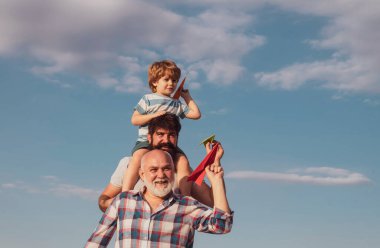 Mutlu dedesi baba ve torun mavi gökyüzü ve bulutlar arka plan üzerinde oyuncak kağıt uçak ile. Üç erkek nesli. Güneşli bir günde basit kağıt uçaklarla oynayan çocuklar