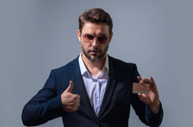 Gri arka planda kredi kartı tutan bir iş adamı. İspanyol adam kredi kartını gösteriyor. Kredi kartı ya da banka kartı. İnternetten alışveriş konsepti. İndirim teklifi, online alışveriş.