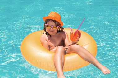 Çocuk havuzda yüzüyor. Yaz tatili. Mutlu çocuk yaz günü havuzda renkli yüzme yüzüğüyle oynuyor. Havuzda yüzen çocuk. Çocuk havuzda dinleniyor, yaz kokteyli içiyor.