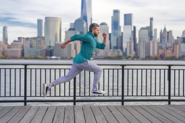 New York 'ta spor kıyafeti giyen bir koşucu. Hareket, sağlıklı koşu. Manhattan yakınlarında koşan olgun bir koşucu. Kaslı sporcu şehirde koşuyor. Spor kıyafetleri. Dışarıda antrenman yapan yakışıklı adam.