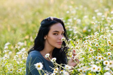 Papatya tarlasından keyif alan güzel bir kadın. Yaz papatya çiçeklerinin çayırında yatan güzel bir dişi. Yazlık çim tarlasında güzel bir kız. Esmer model ve yaz yeşili doğa, uyum kavramı.