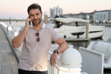 Büyük şehirde telefonda konuşan yakışıklı bir adamın portresi. Sokakta telefonla konuşan, günlük kıyafetli seksi bir adam. Şehir yaşam tarzında başarılı bir erkek model. İş telefonu görüşmesi