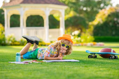 Yaratıcılık çocuk konsepti. Okul çocuğu yaz parkında resim çiziyor. Küçük bir ressam açık havada resim çizer. Dışarıda oynayan mutlu çocuk. Yaz teması çiziliyor