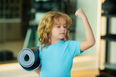 Sportif çocuk spor salonunda yoga minderi tutuyor. Yoga çocuk konsepti. Pazılarını gösteren güçlü, genç bir çocuk. Spor sporu konsepti