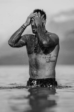 Adam gölde rahatladı. Yaz plajında çıplak gövdeli yakışıklı bir adam. Alps gölündeki seksi bir adamın portresi. Özgürlük ve seyahat macerası. Seksi gezgin İsviçre 'de manzaranın tadını çıkarıyor