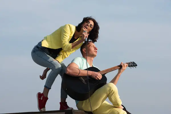 Excited sexy couple enjoy music with microphones and guitar. Sexy couple singing outdoor. Love music. Couple in love singing and playing guitar. Music and Musical instrument concept. Outdoor music