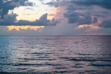 Gökyüzü ve bulutların arasından güneş batarken deniz batıyor. Okyanus ve gökyüzü arkaplanı, deniz manzarası.