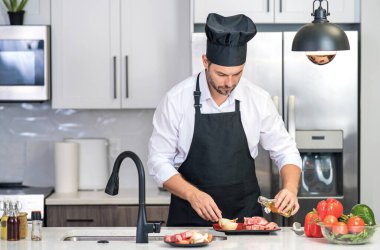 Şef olgun aşçı mutfakta önlük giyer. Yakışıklı adam mutfakta yemek hazırlıyor. Lezzetli yemek pişiren adam. Mutfakta et ve sebzeli bir adam. Mutfakta önlüklü sıradan bir adamın portresi.