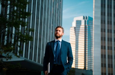 İş adamının elinde dizüstü bilgisayar vardı. İş yerinin yakınında duruyordu.