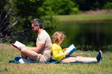 Babam oğluyla açık havada parkta bir kitap okudu. Baba ve çocuk dışarıda yeşil doğa hakkında bir şeyler okuyorlar. Baba ve çocuk kitabı okuyorlar yaz parkında. Aile doğada kitap okuyor.