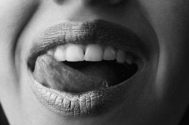 Dişi dolgun dudakları altınla kapat. Altın parıltılı ruj. Seksi dil yalayan dudaklar. Şehvetli, mutlu, gülümseyen kadın ağzı. Parlak altın dudaklar. Altın boyalı altın dudaklar veya metalik ruj