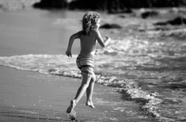 Deniz kıyısına yakın sularda koşan bir çocuk. Bir çocuk deniz kıyısında koşuyor. Çocukların geri kalanı yaz tatilinde.
