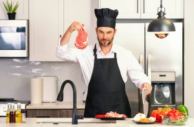 Şef olgun aşçı mutfakta önlük giyer. Yakışıklı adam mutfakta yemek hazırlıyor. Lezzetli yemek pişiren adam. Mutfakta et ve sebzeli bir adam. Mutfakta önlüklü sıradan bir adamın portresi.