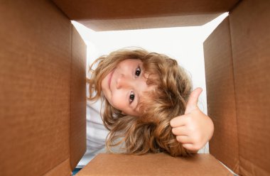 Şaşırmış çocuk, başparmağını kaldırmış, kutusunu açıyor ve içine bakıyor. Paket, teslimat, sürpriz, çocuk için hediye. Çocuk duyguları ve çocuk yüz ifadeleri