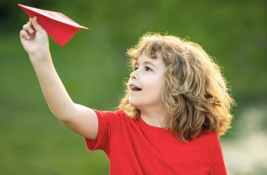 Küçük çocuk kağıt uçak tutuyor. Oyuncak uçak çocukların elinde. Mutlu çocuk eğiliyor ve sarı kağıt uçak fırlatıyor. Çocuk kağıt uçakla oynuyor. Kağıt uçakla oynayan çocuk