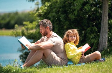 Babam oğluyla açık havada parkta bir kitap okudu. Baba ve çocuk dışarıda yeşil doğa hakkında bir şeyler okuyorlar. Baba ve çocuk kitabı okuyorlar yaz parkında. Aile doğada kitap okuyor.